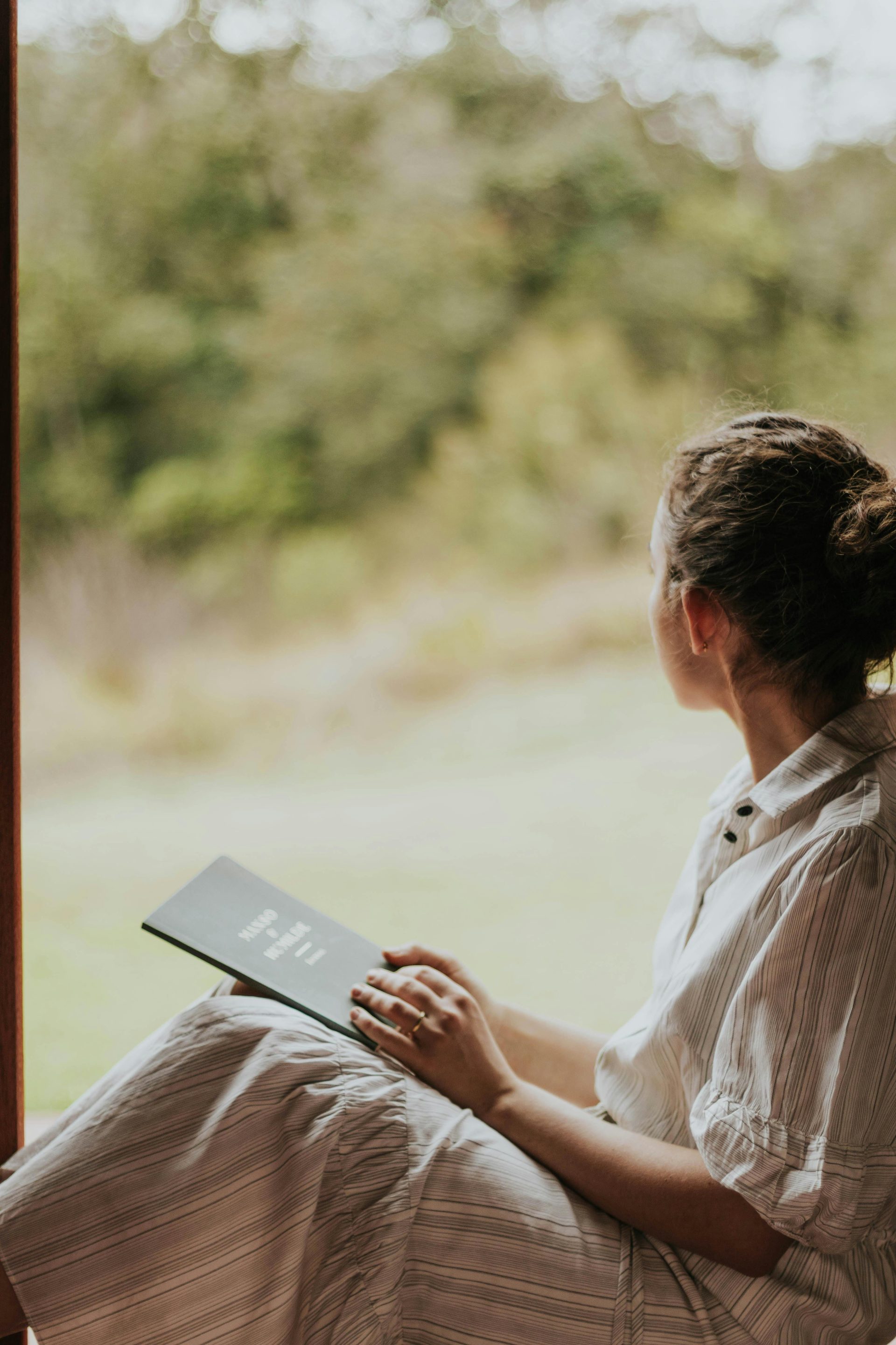 A woman sitting on a window sill reading a book